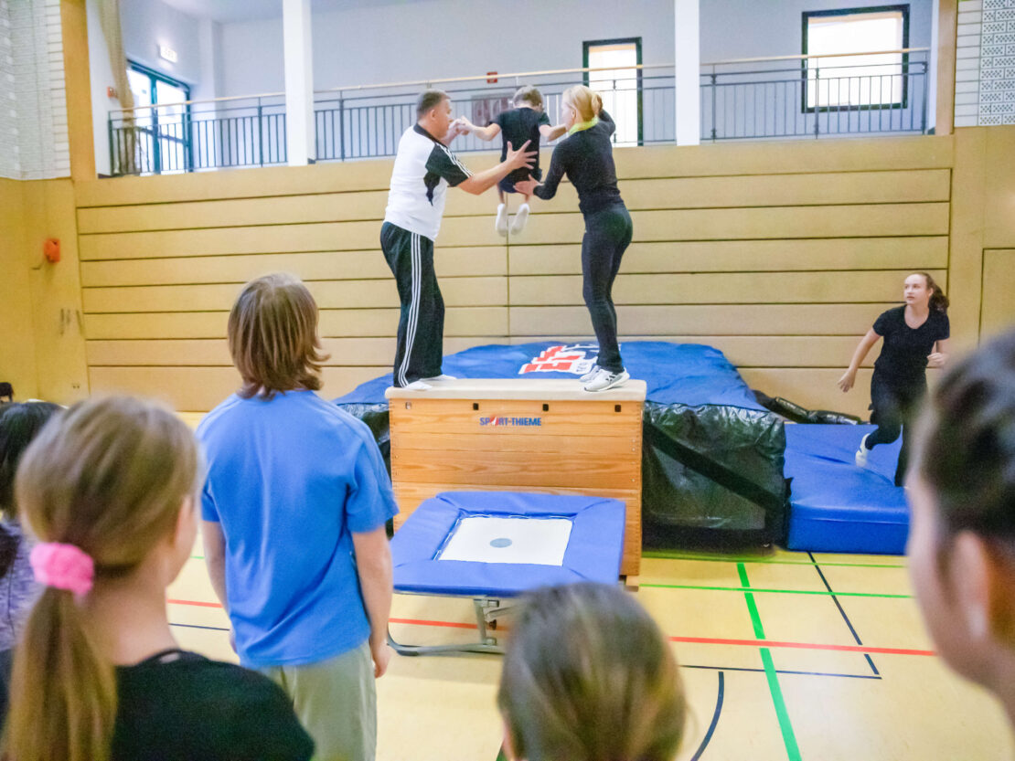 a coach and a parent helping a child practice on a gymnastics air bag